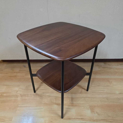 Wooden side table with a single shelf on a wooden floor.