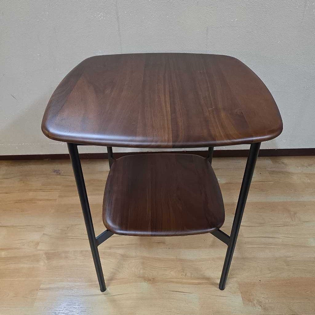Wooden side table with a shelf on a wooden floor against a plain wall