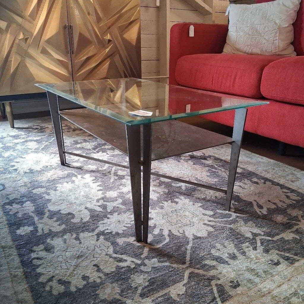 Glass coffee table in a living room with a red sofa and abstract wall art.