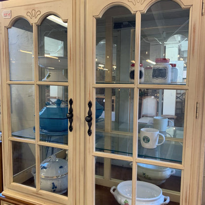 Beige glass-fronted cabinet with various items inside, including a Starbucks mug.