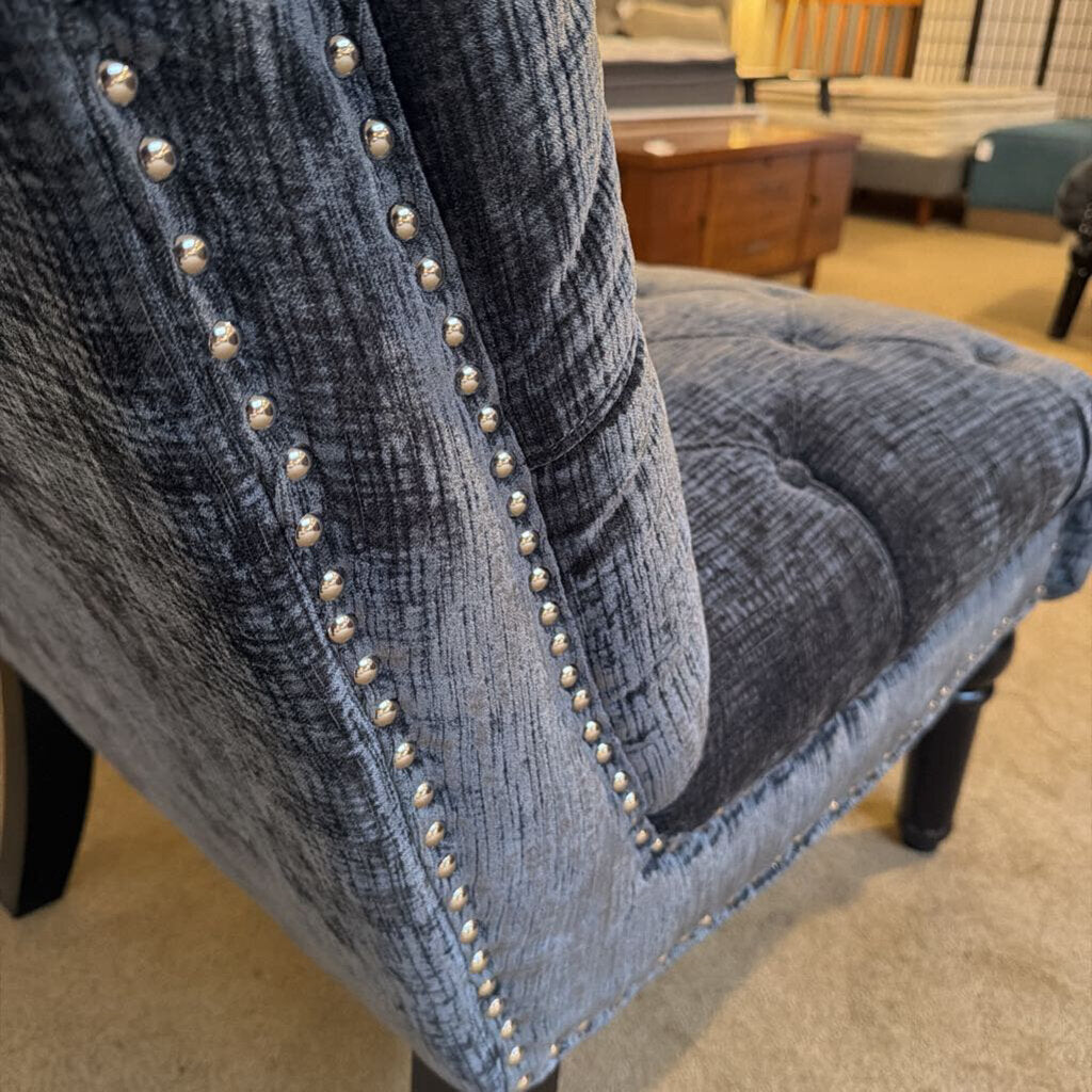 Close-up of a blue upholstered chair with nailhead trim in a room setting.