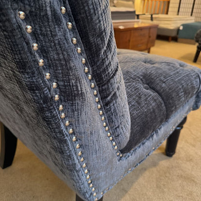 Close-up of a blue upholstered chair with nailhead trim in a room setting.