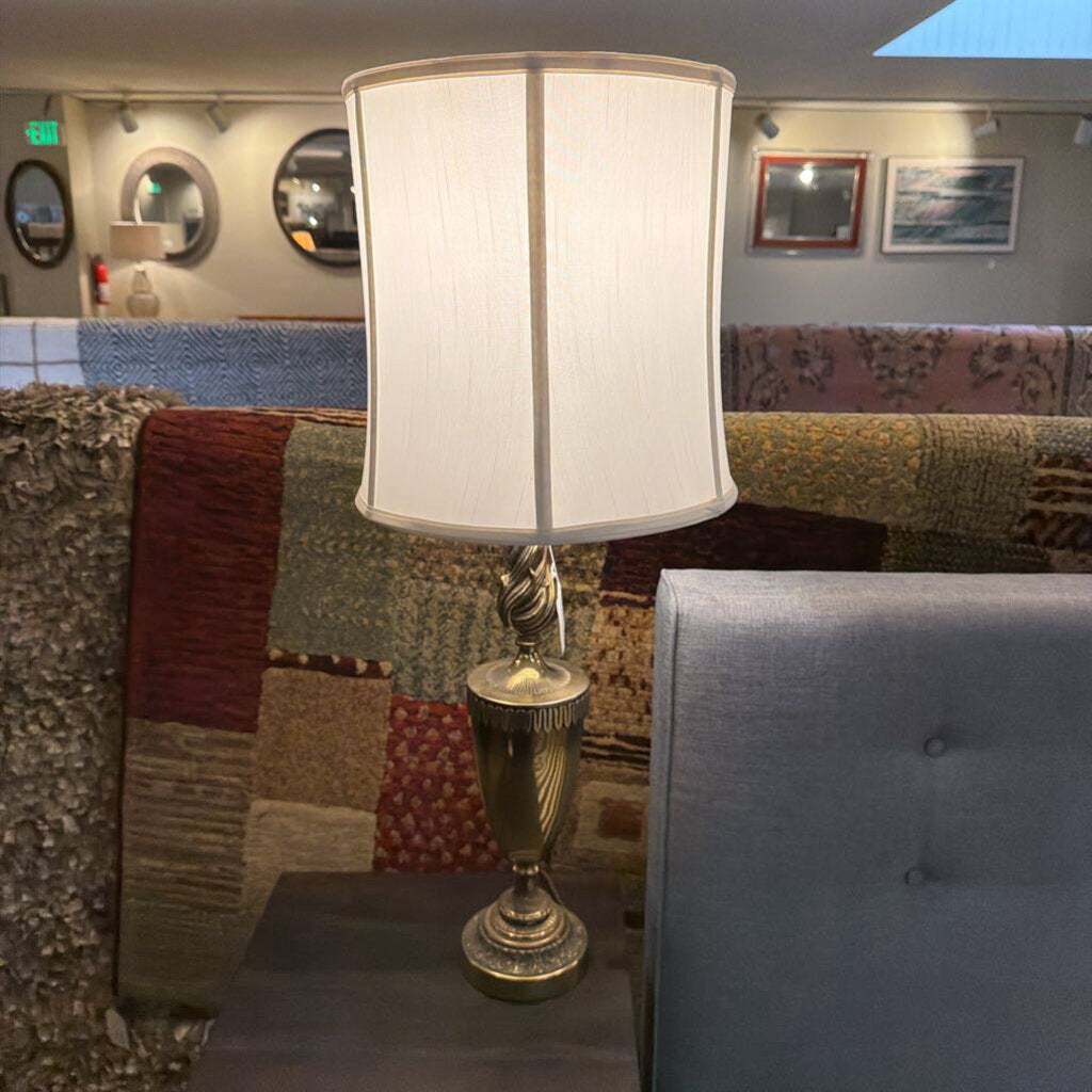 Decorative lamp with a white shade on a table in a room with patterned rugs and a couch.