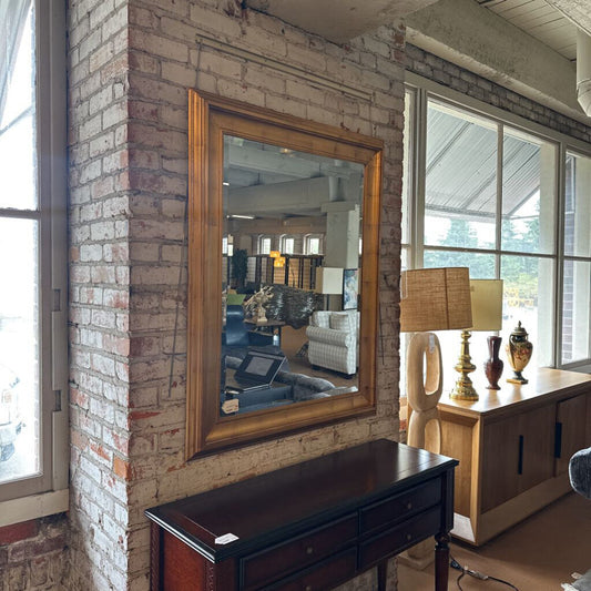 Large mirror with wooden frame on a brick wall in a room with furniture and decor.
