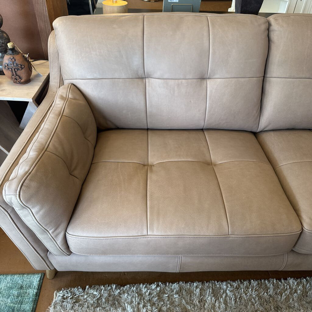 Beige leather sofa in a room with a small table and decorative items.