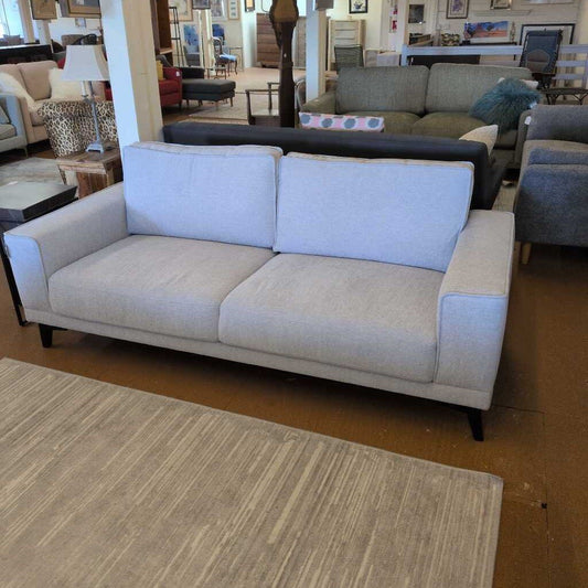 Light gray sofa in a showroom setting with other furniture.