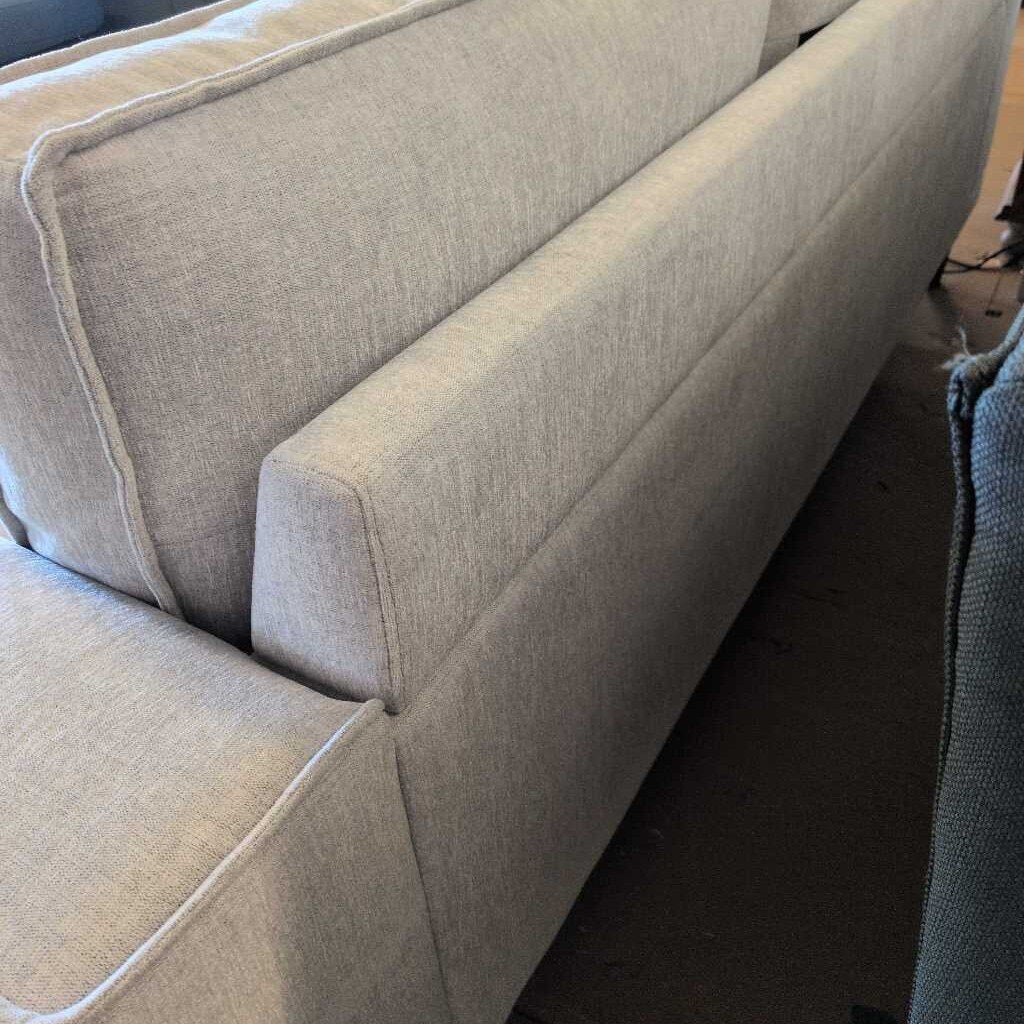 Beige sofa with a focus on the armrest and backrest.