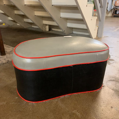 Oval-shaped ottoman with gray top and black base in a room with stairs.