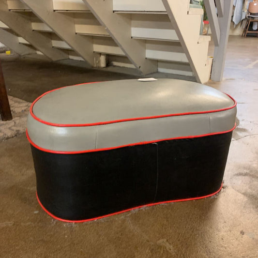 Oval-shaped ottoman with gray top and black base in a room with stairs.