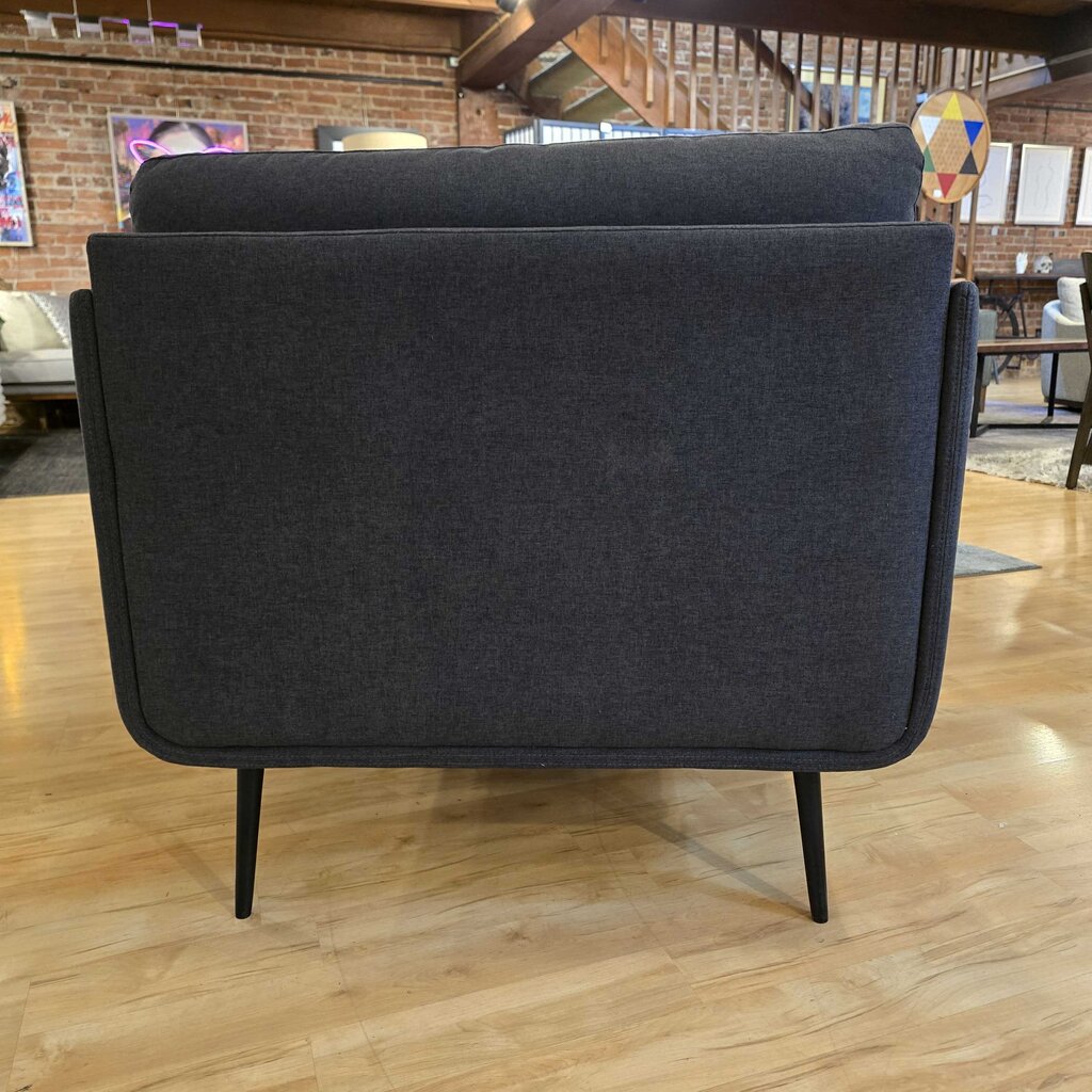 Dark gray upholstered chair on a wooden floor with a blurred indoor background