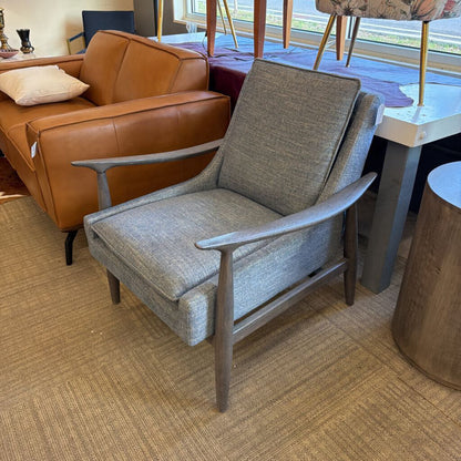 Gray armchair in a room with a brown leather sofa and a table.
