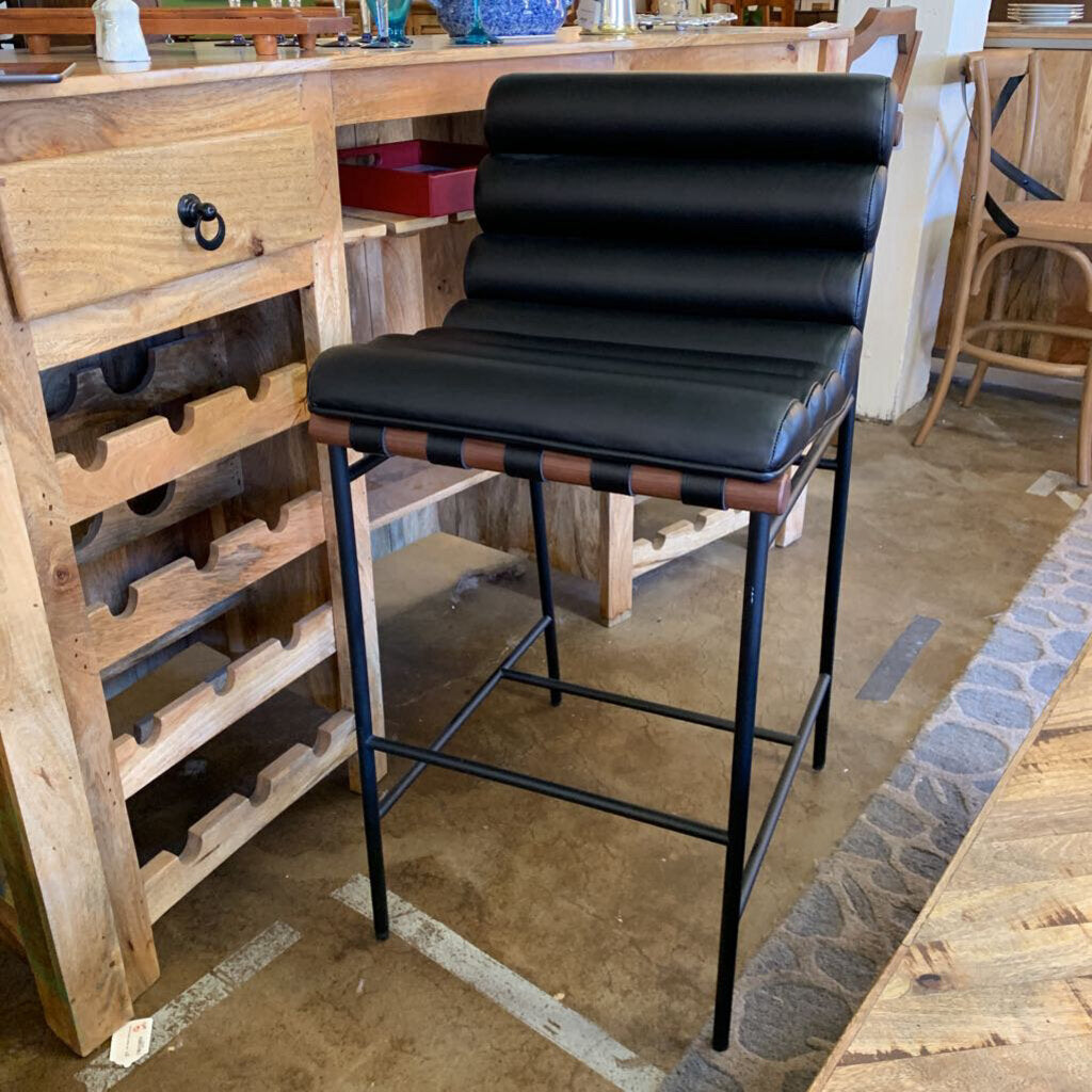 Black bar stool in a rustic kitchen setting with wooden cabinets and a stone floor.