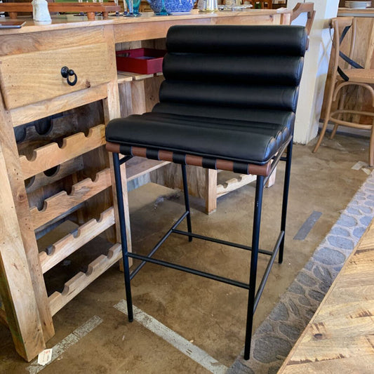 Black bar stool in a rustic kitchen setting with wooden cabinets and a stone floor.