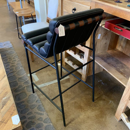 Bar stool with black cushioned seat and backrest in a store setting.