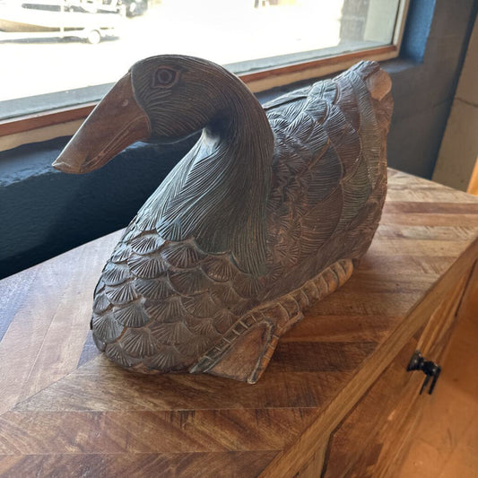 Wooden duck sculpture on a wooden surface with a window in the background