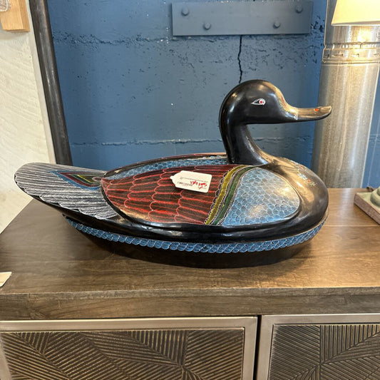 Decorative duck-shaped bowl on a wooden surface with a blue wall in the background
