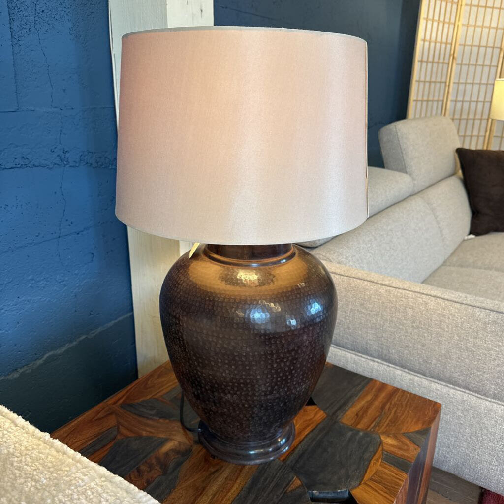 Decorative lamp with a textured base on a wooden side table next to a gray sofa.