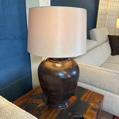 Decorative lamp with a textured base on a wooden side table next to a gray sofa.