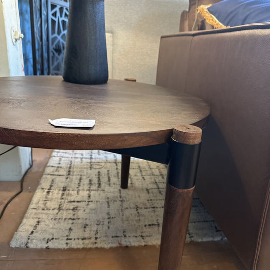 Wooden side table with a remote control next to a brown sofa in a living room.