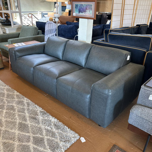 Gray leather sofa in a showroom setting with other furniture and decor.