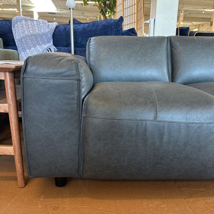 Gray leather sofa in a showroom setting with wooden floor and furniture.