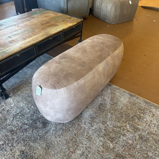 Oval-shaped brown cushion on a textured floor with a wooden table in the background.