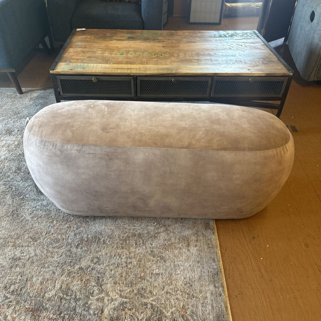 Oval-shaped beige ottoman on a carpeted floor with a wooden coffee table in the background.