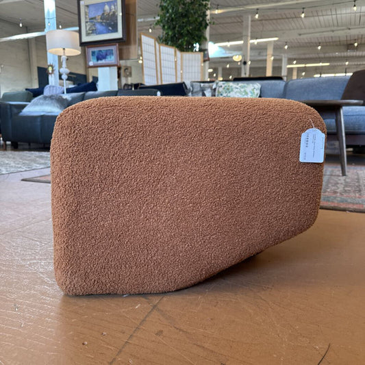 Brown textured pillow with a tag on a wooden floor in a furniture store.