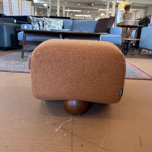 Brown textured ottoman on a wooden floor with furniture in the background