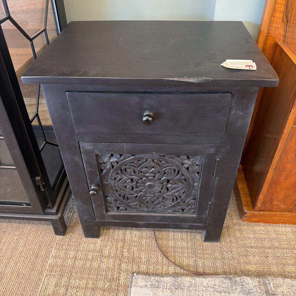 Dark wooden nightstand with decorative carvings on a carpeted floor.