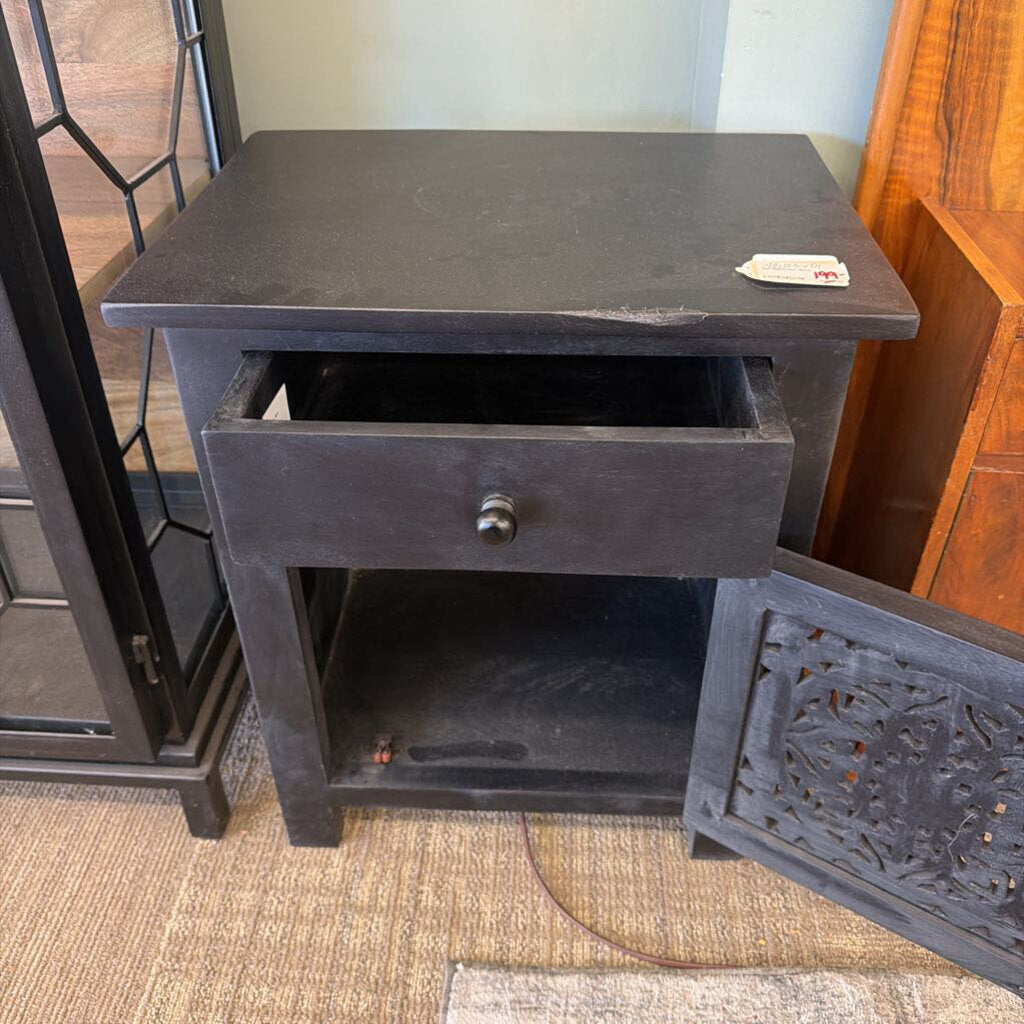 Black nightstand with a drawer on a carpeted floor