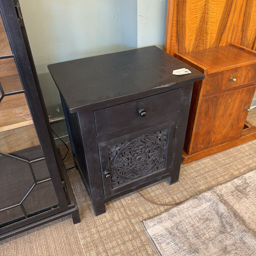 Dark wooden nightstand with decorative carvings on a carpeted floor.