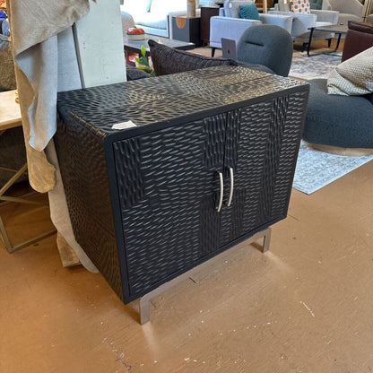 Black woven storage chest on a wooden floor with blurred furniture in the background