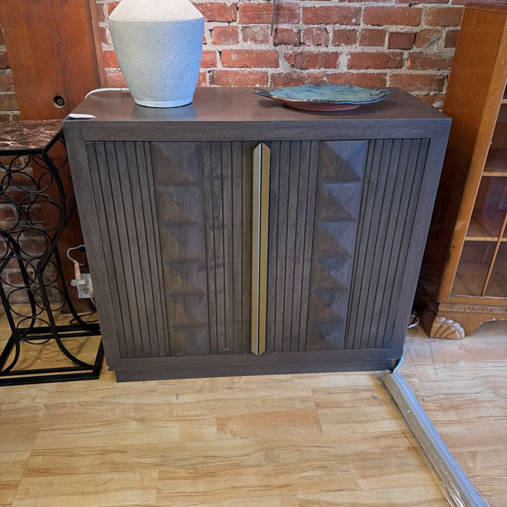 Wooden cabinet with decorative elements against a brick wall.