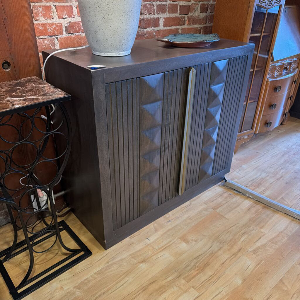 Wooden cabinet with decorative design on a wooden floor against a brick wall.