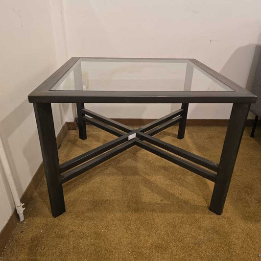 Glass-top table with black metal frame on a carpeted floor against a white wall.