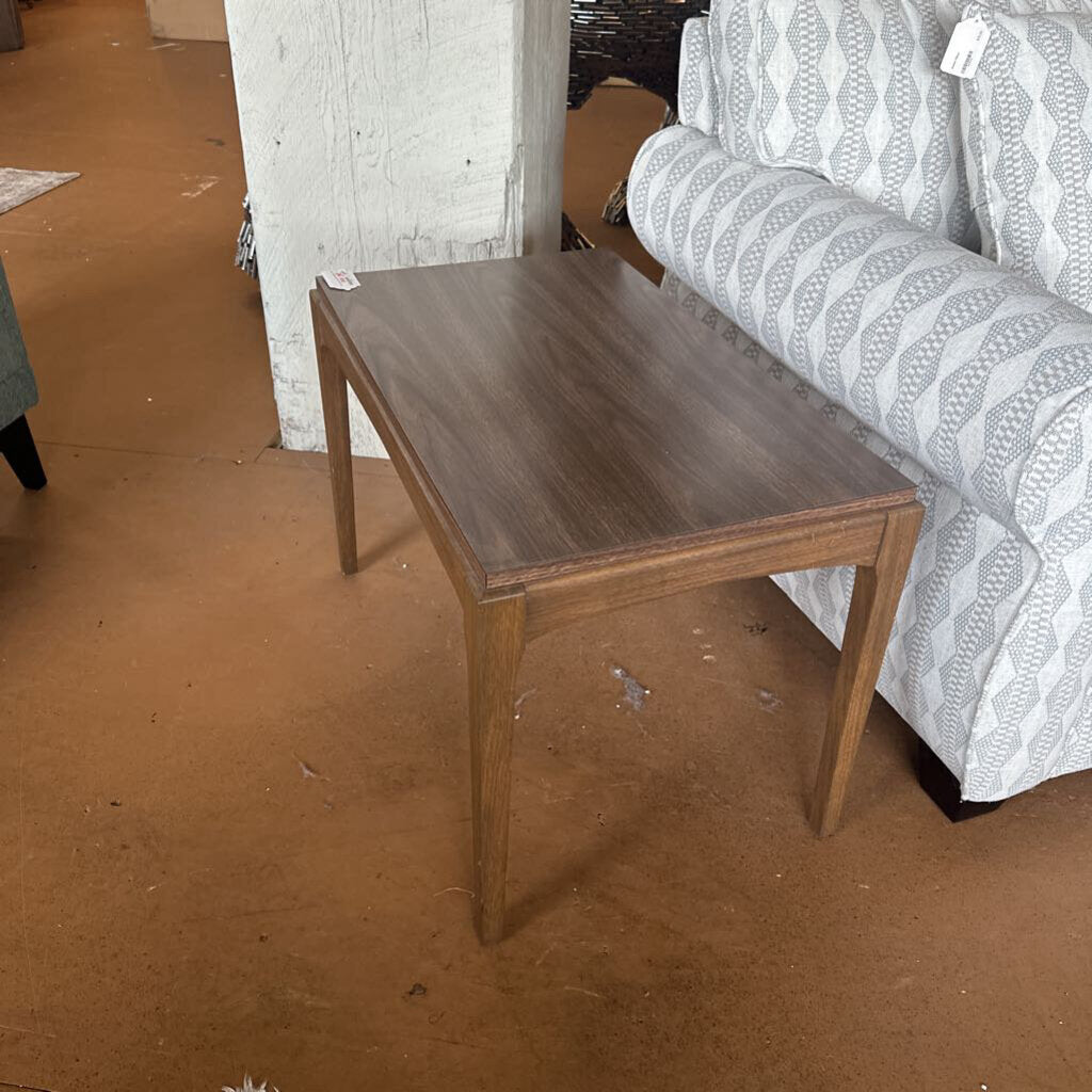 Wooden side table in a room with furniture and flooring.