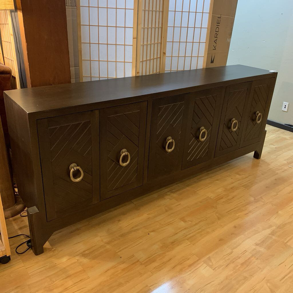 Dark wooden sideboard with geometric designs and gold ring handles on a wooden floor.