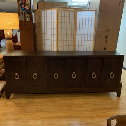 Dark wooden sideboard with decorative handles in a room with cardboard boxes and a lamp.