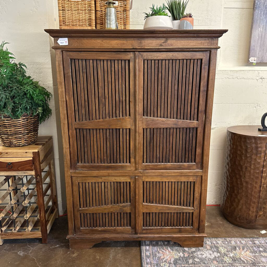 Wooden cabinet with slatted doors in a room with plants and furniture.