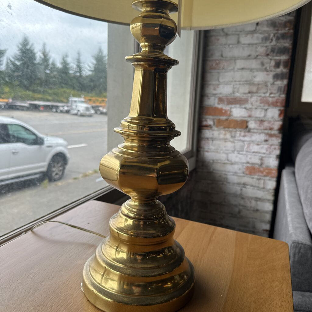Brass lamp on a wooden surface with a window and outdoor view in the background
