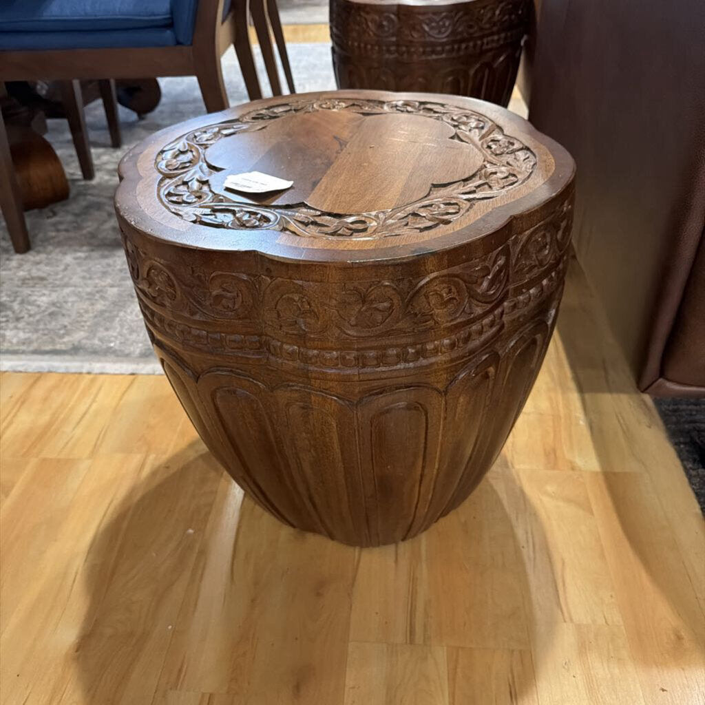 Decorative wooden stool with intricate carvings on a wooden floor.