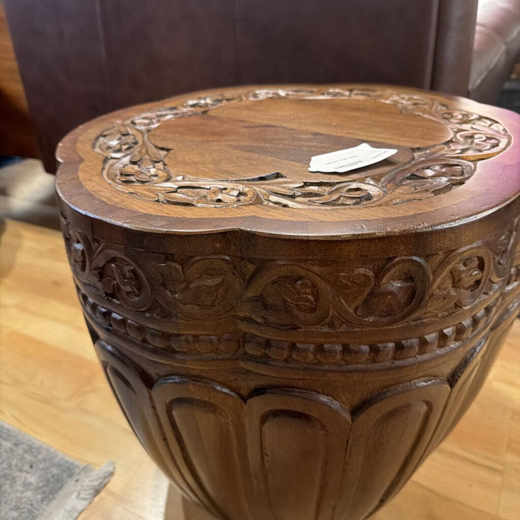 Carved wooden stool with intricate patterns on a wooden floor.