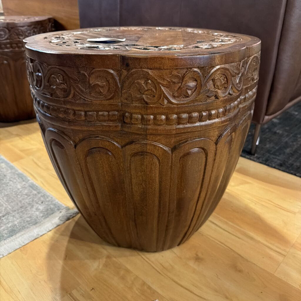 Decorative wooden stool with intricate carvings on a wooden floor.