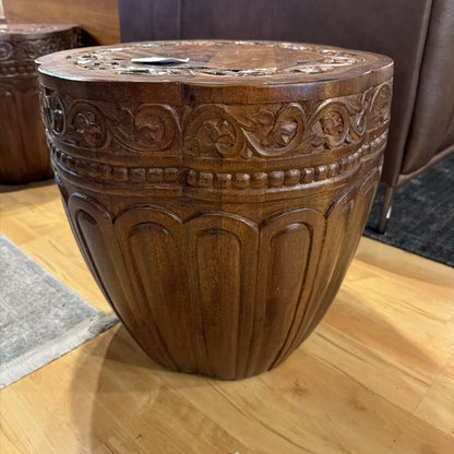 Decorative wooden stool with intricate carvings on a wooden floor.