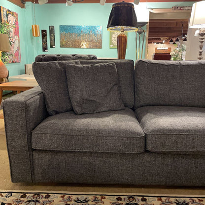 Gray sectional sofa in a living room setting with a teal wall and decorative items.