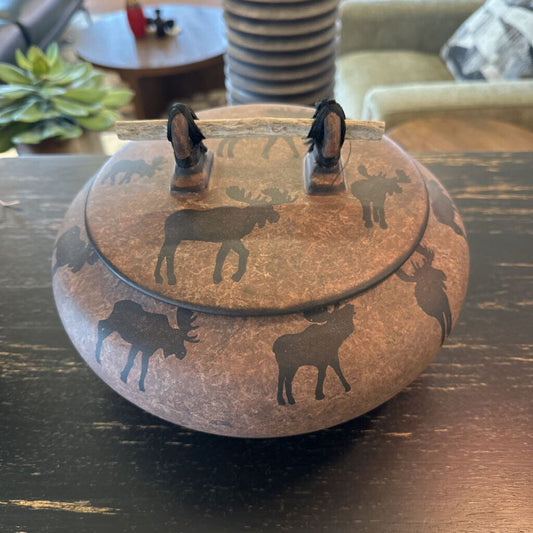 Decorative pot with moose designs on a wooden surface