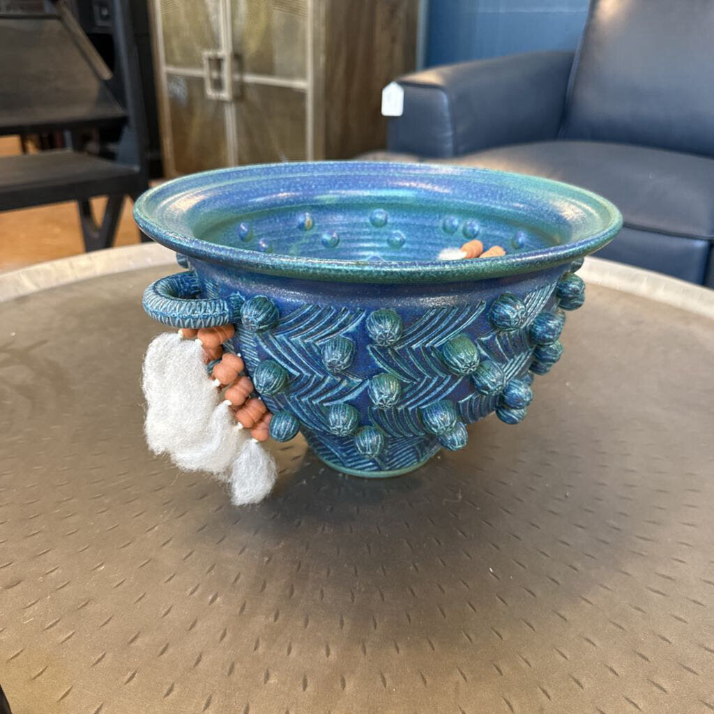 Blue textured planter on a round metal table with a chair and cabinet in the background.