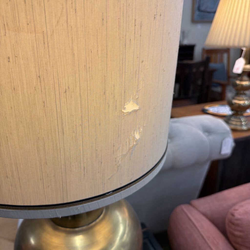 Close-up of a lamp with a beige shade and gold base in an indoor setting.