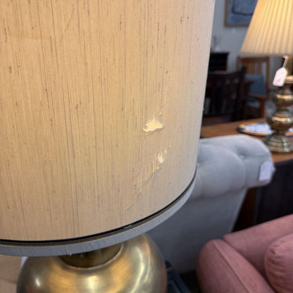 Close-up of a lamp with a beige shade and gold base in an indoor setting.